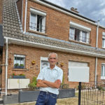 Un homme à la retraite pose devant sa maison équipée de panneaux solaires