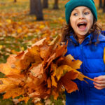 Une petite fille dans une forêt en automne tient un bouquet de feuilles mortes