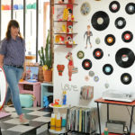 Une femme entre dans un salon à la déco très chargée, remplie d'objets en plastique et de vinyles au mur