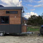 Une tiny house au milieu des champs à côté d'un tracteur qui l'a remorquée