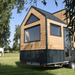 Une belle tiny house en bois dans un pré avec un cheval