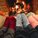 Les pieds d'une famille avec des chaussettes épaisses devant un feu de cheminée