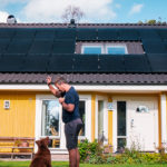 Un homme joue avec son chien devant sa maison équipée de panneaux solaires